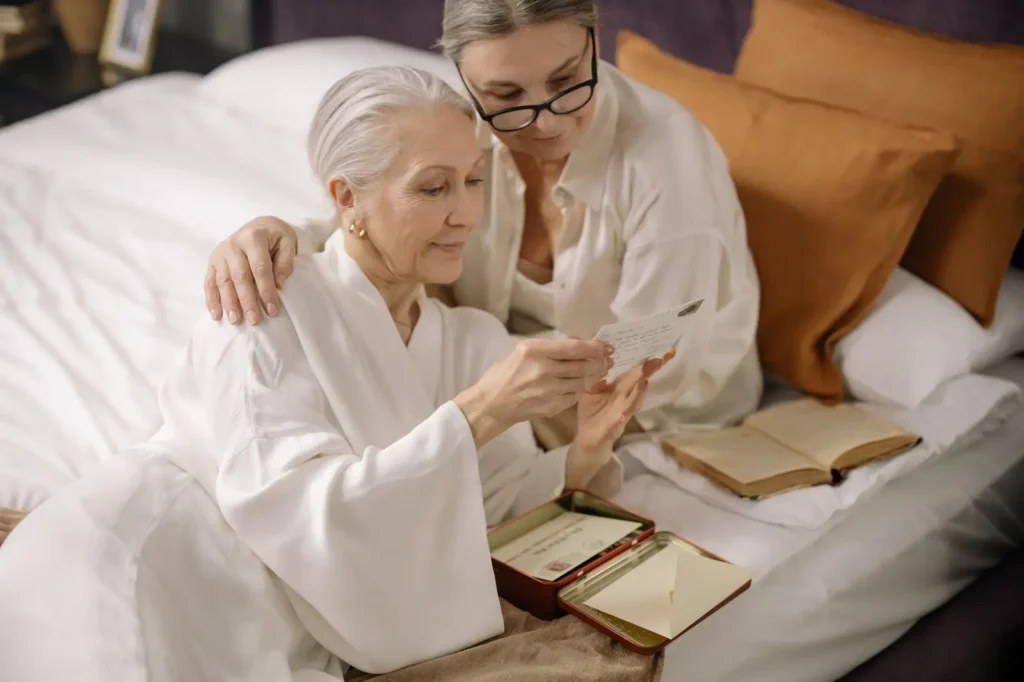 An older woman and her daughter reading papers on a bed in a bright room