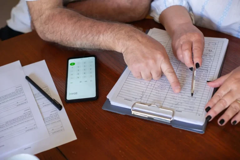 Two people going over a printed form with a pen and a phone calculator