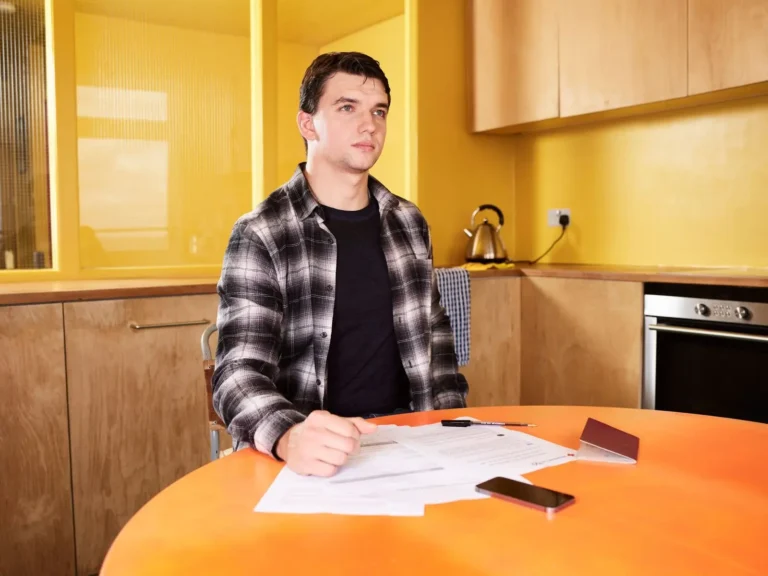 A young man at a kitchen table with papers and a phone