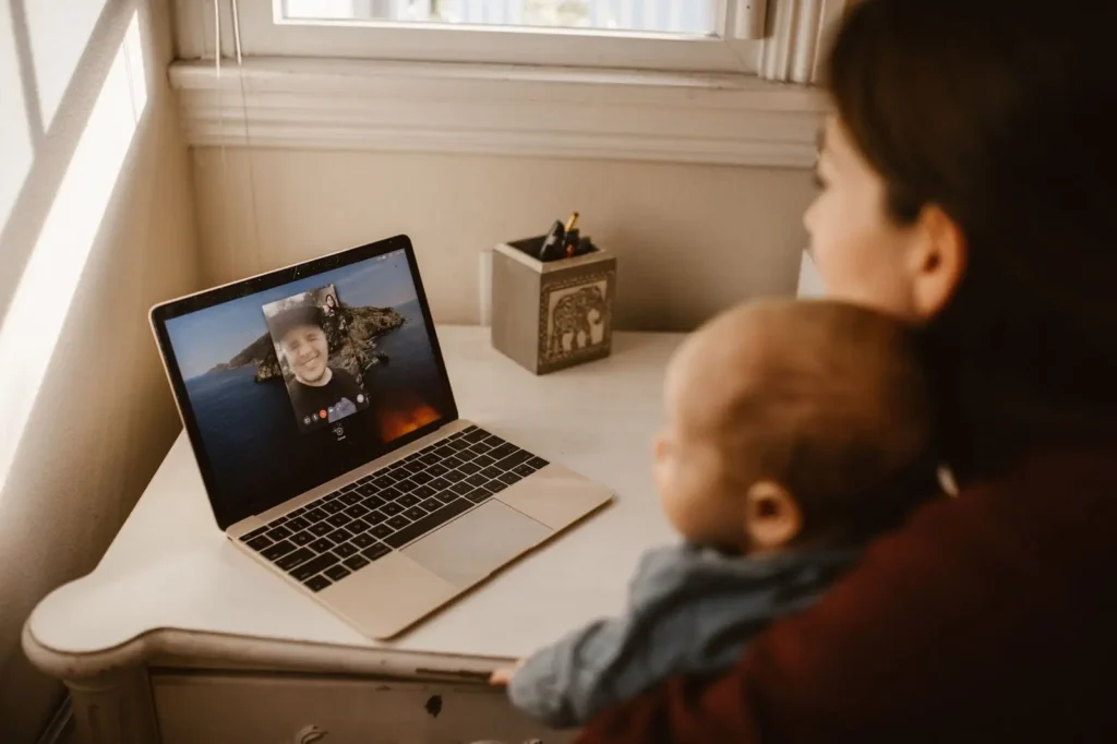 A mother holding her baby in front of a laptop on a video call