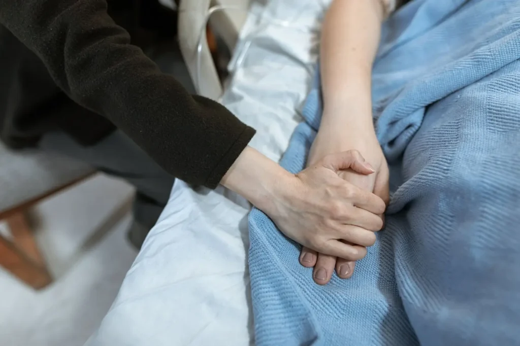A hand resting on another hand on a hospital blanket