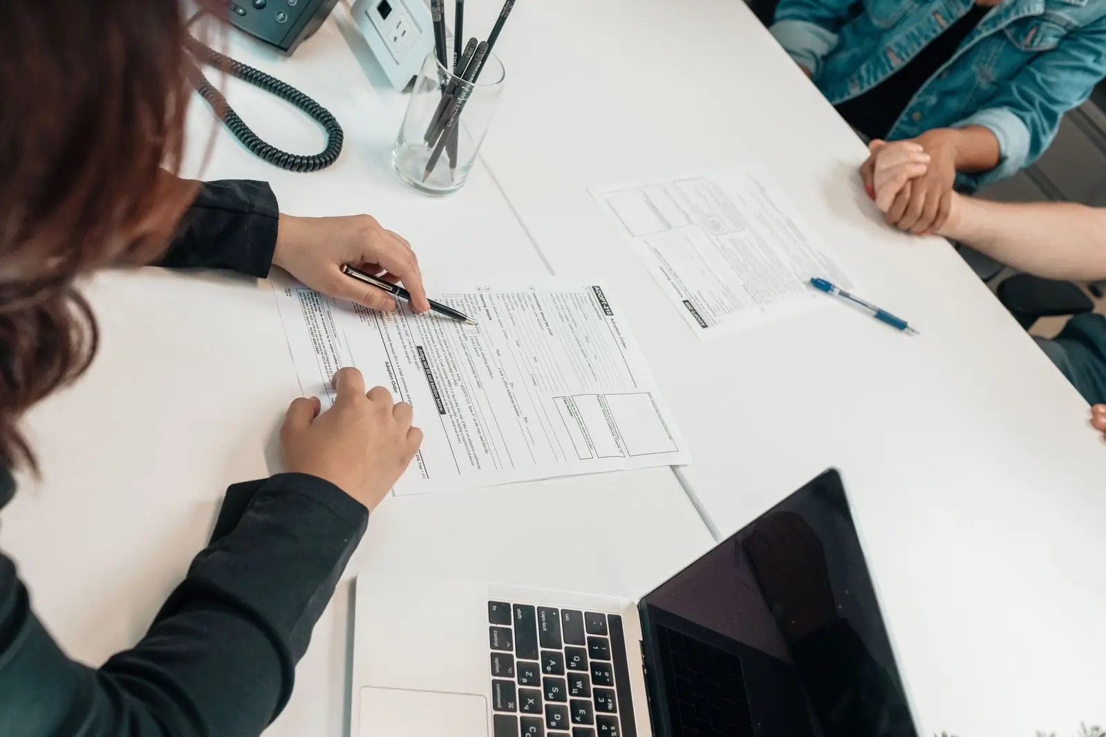 Hands filling in a printed form on a white desk beside a laptop