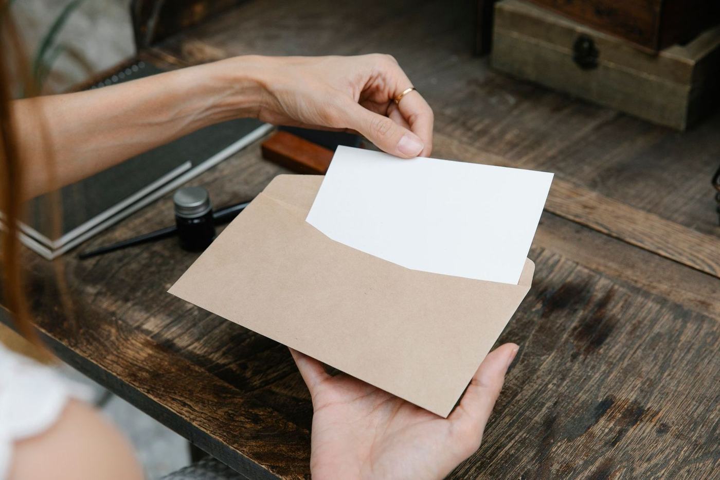 Two hands passing a brown envelope with a white card across a wooden desk