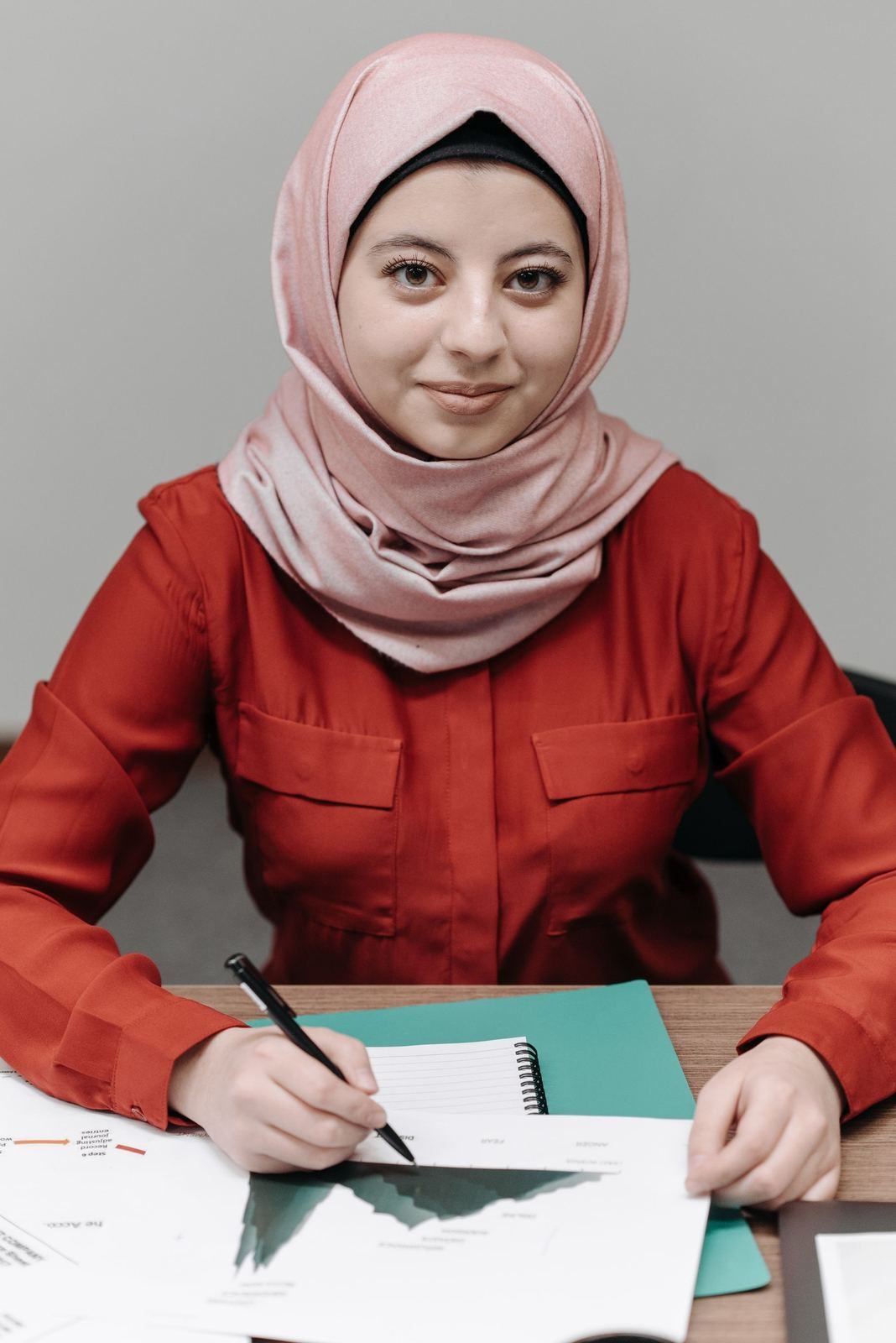 Woman in a pink hijab signing a document at an office table