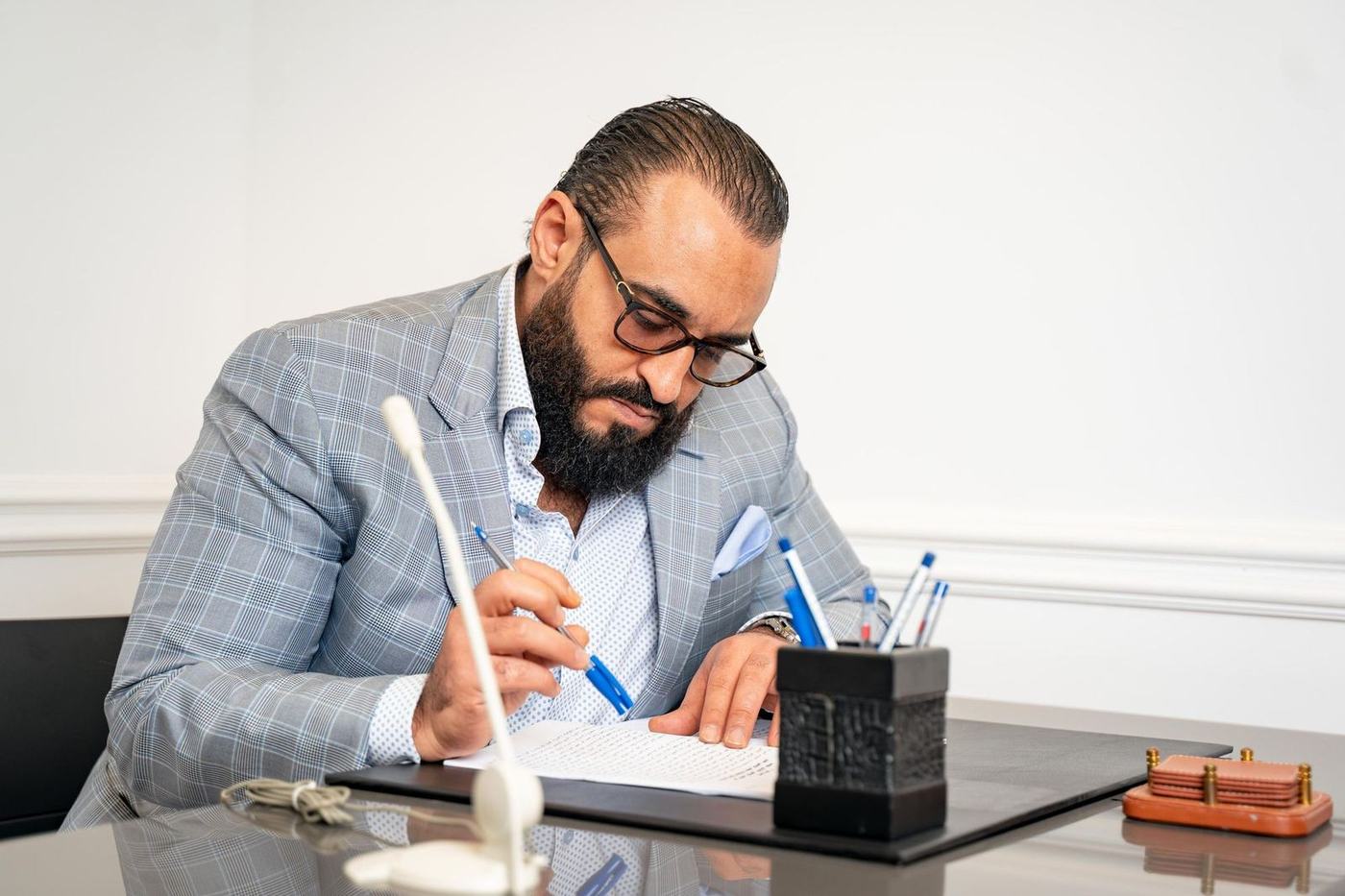 Bearded man in a grey checked jacket signing a document at a desk