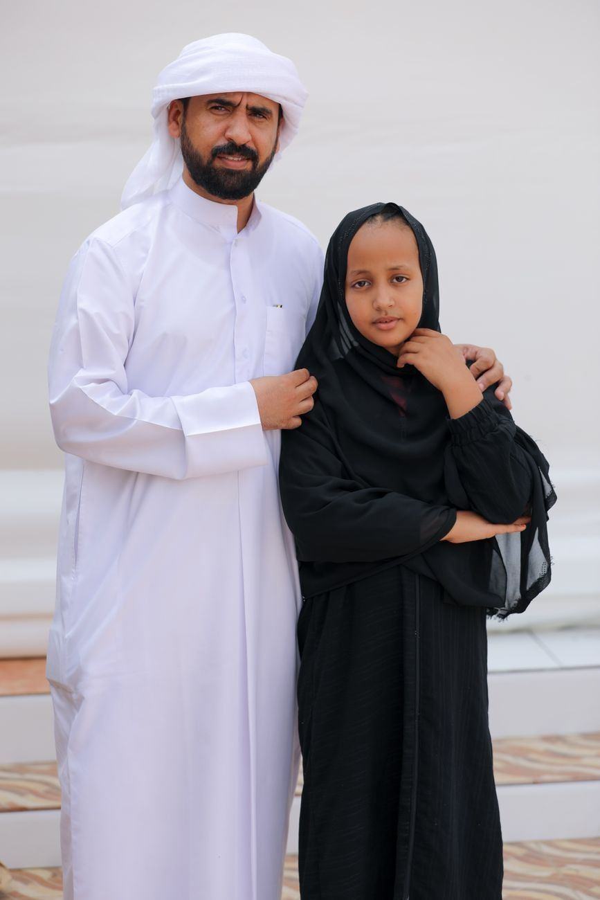 Father in a white kandura standing with his daughter in a black abaya