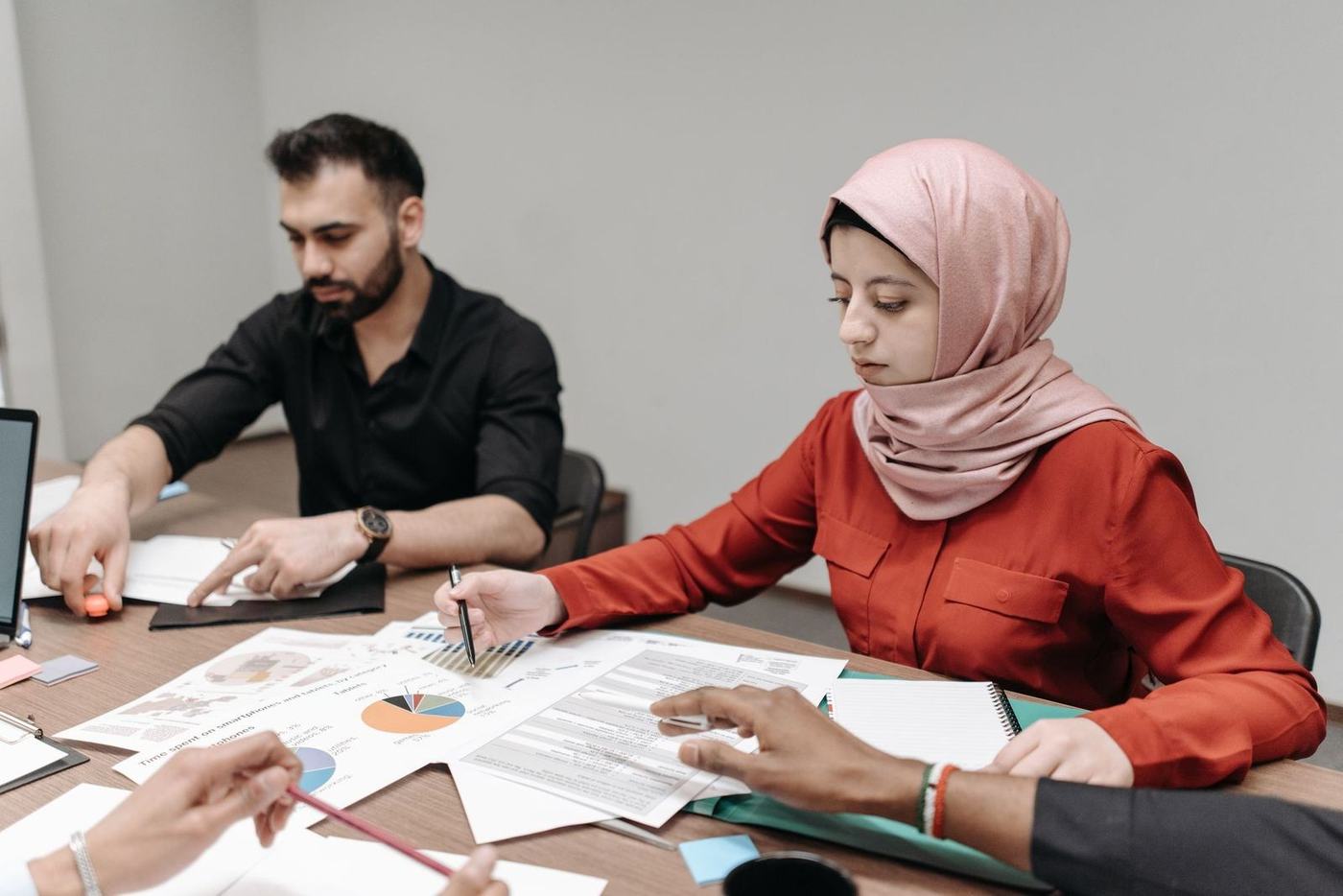 Woman in a pink hijab and a colleague reviewing printed documents at a meeting table