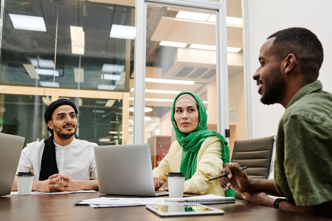 Woman in a green hijab in a meeting with two male colleagues at a table with laptops