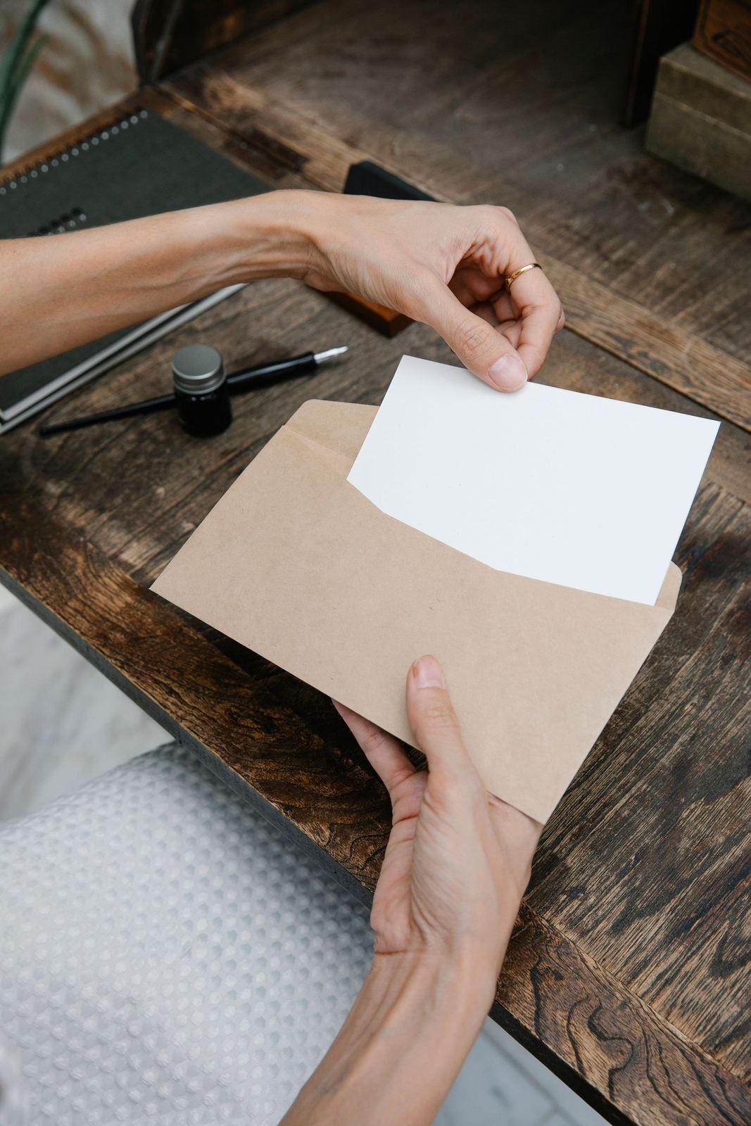 Hands taking a white card out of a brown envelope at a desk