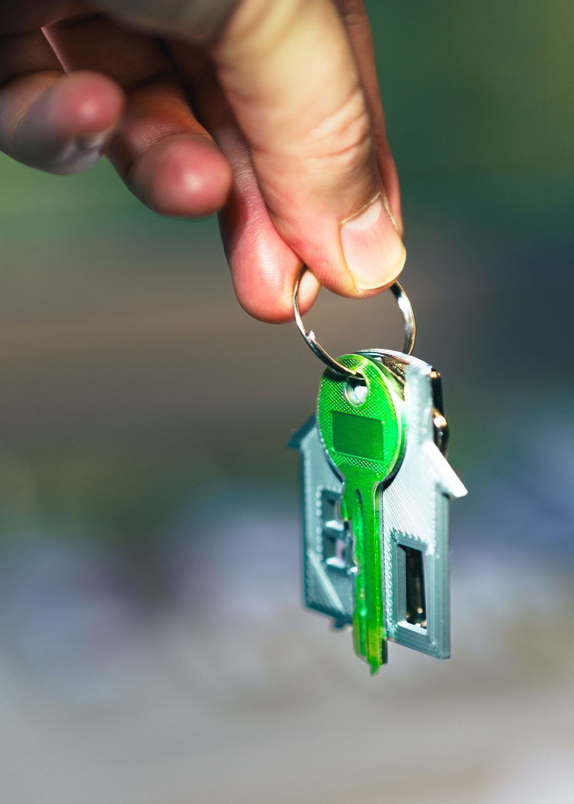 Hand holding a key on a small house shaped key ring