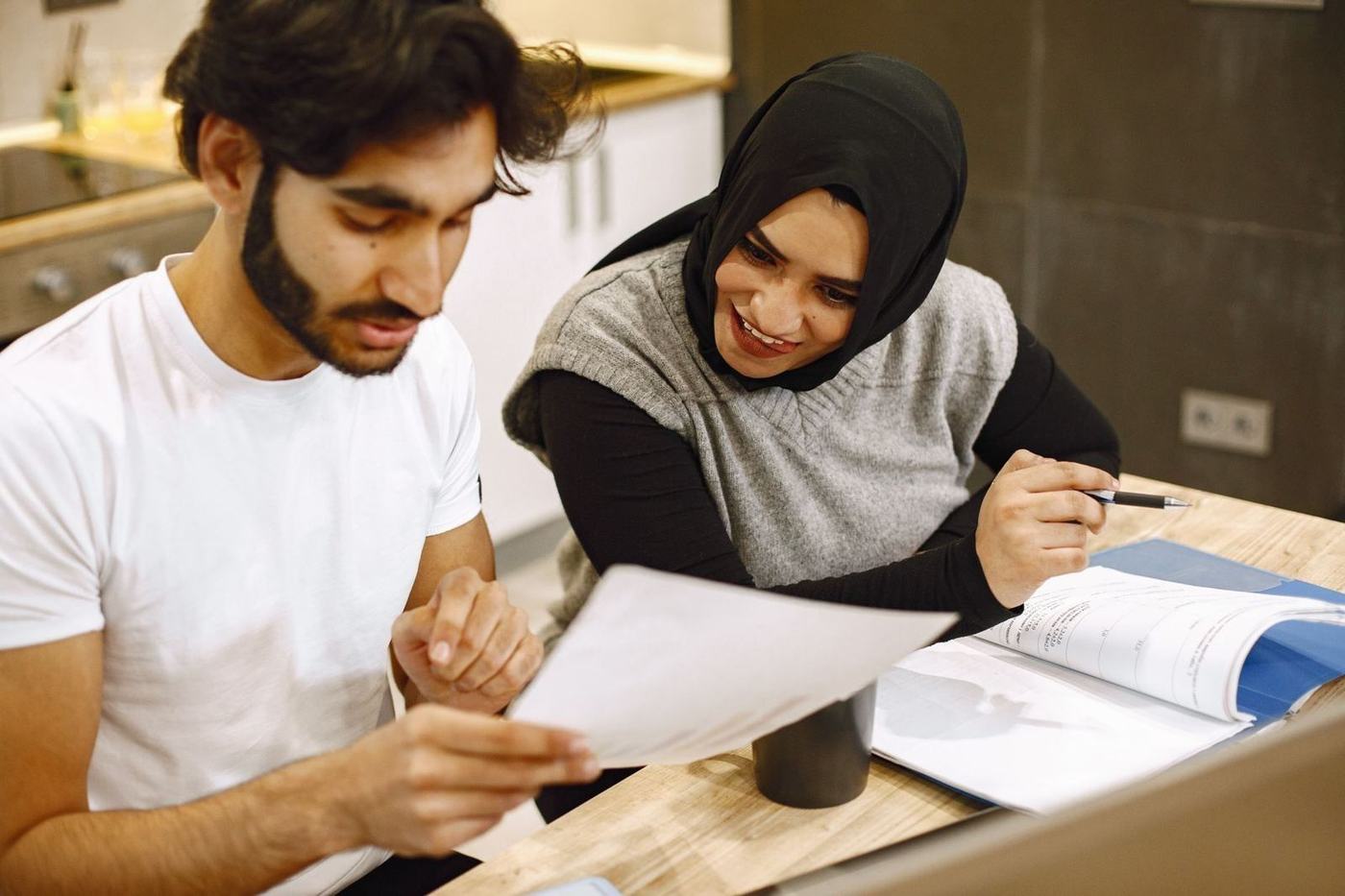 Man and woman in a hijab going through papers together at a table at home