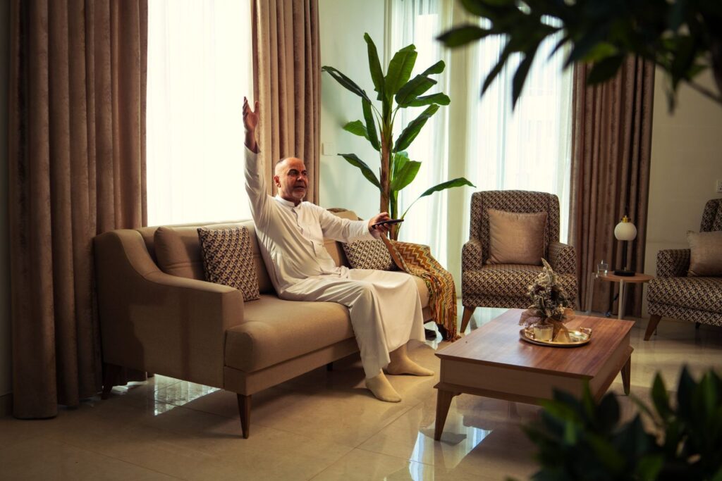 An older man in a white kandura sitting on the sofa in his living room