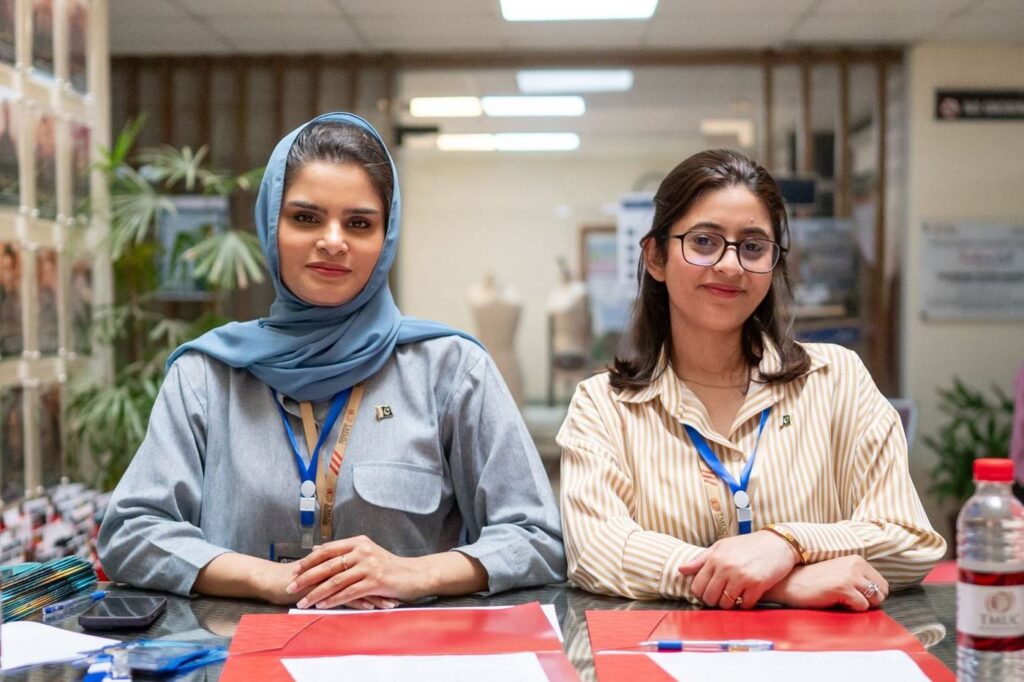 Two women in an office sitting side by side at a desk with papers in front of them