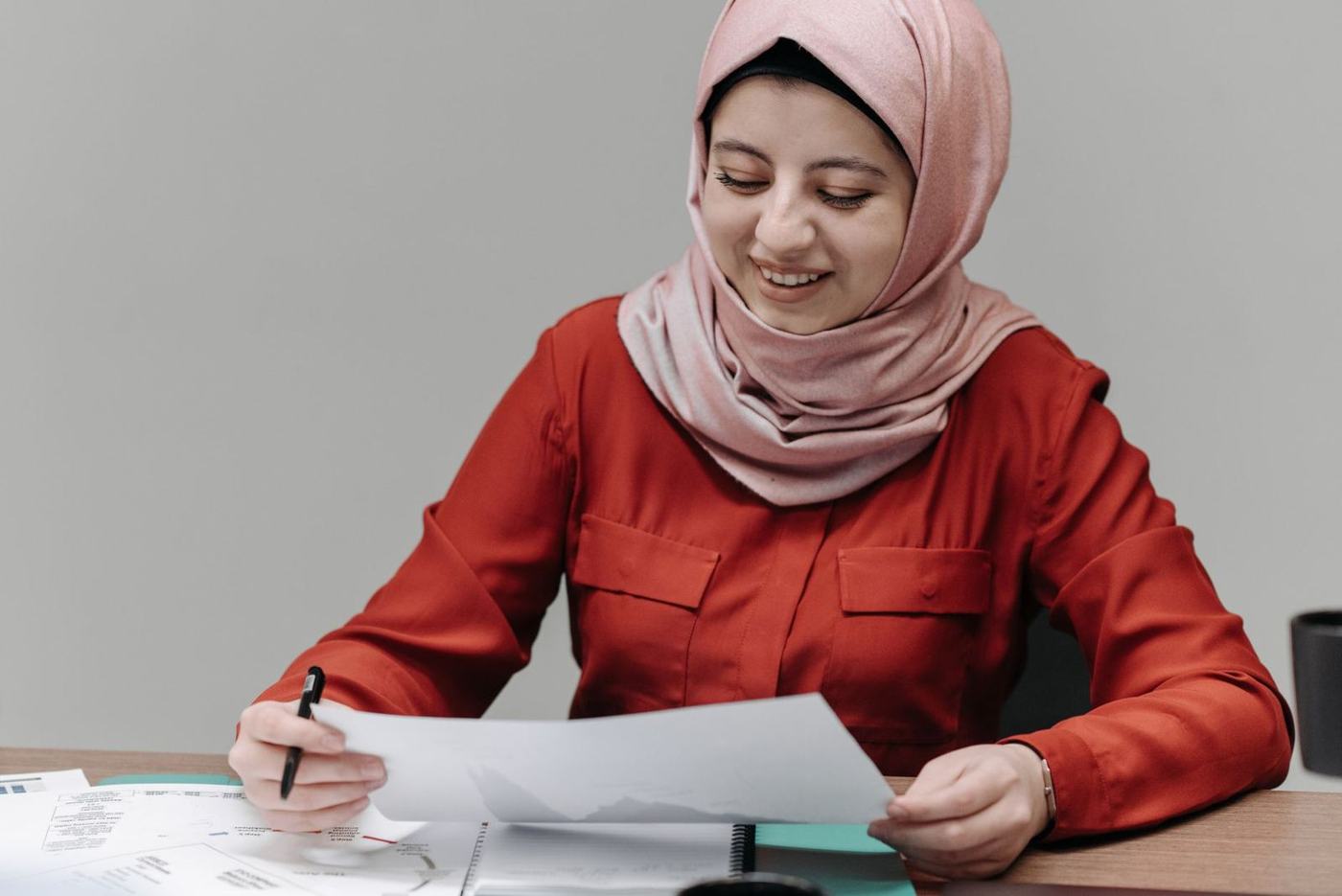 A woman in a pink hijab filling in a printed form with a pen