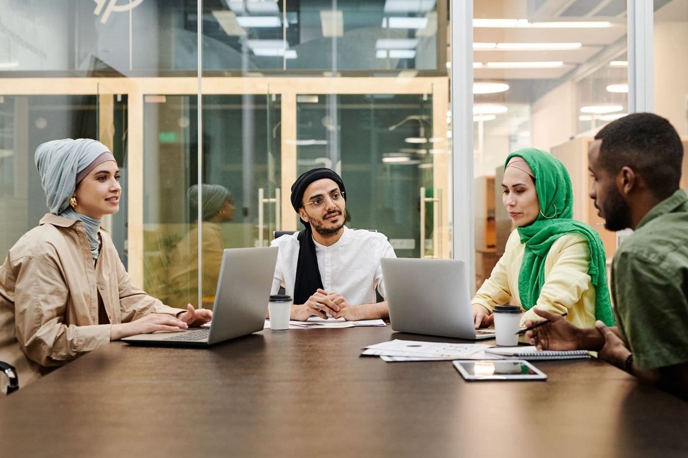 أربعة زملاء إلى طاولة اجتماعات أمام حواسيب محمولة، بينهم امرأتان بالحجاب
