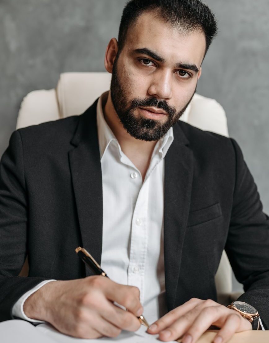 A man in a dark suit signing a document at his desk