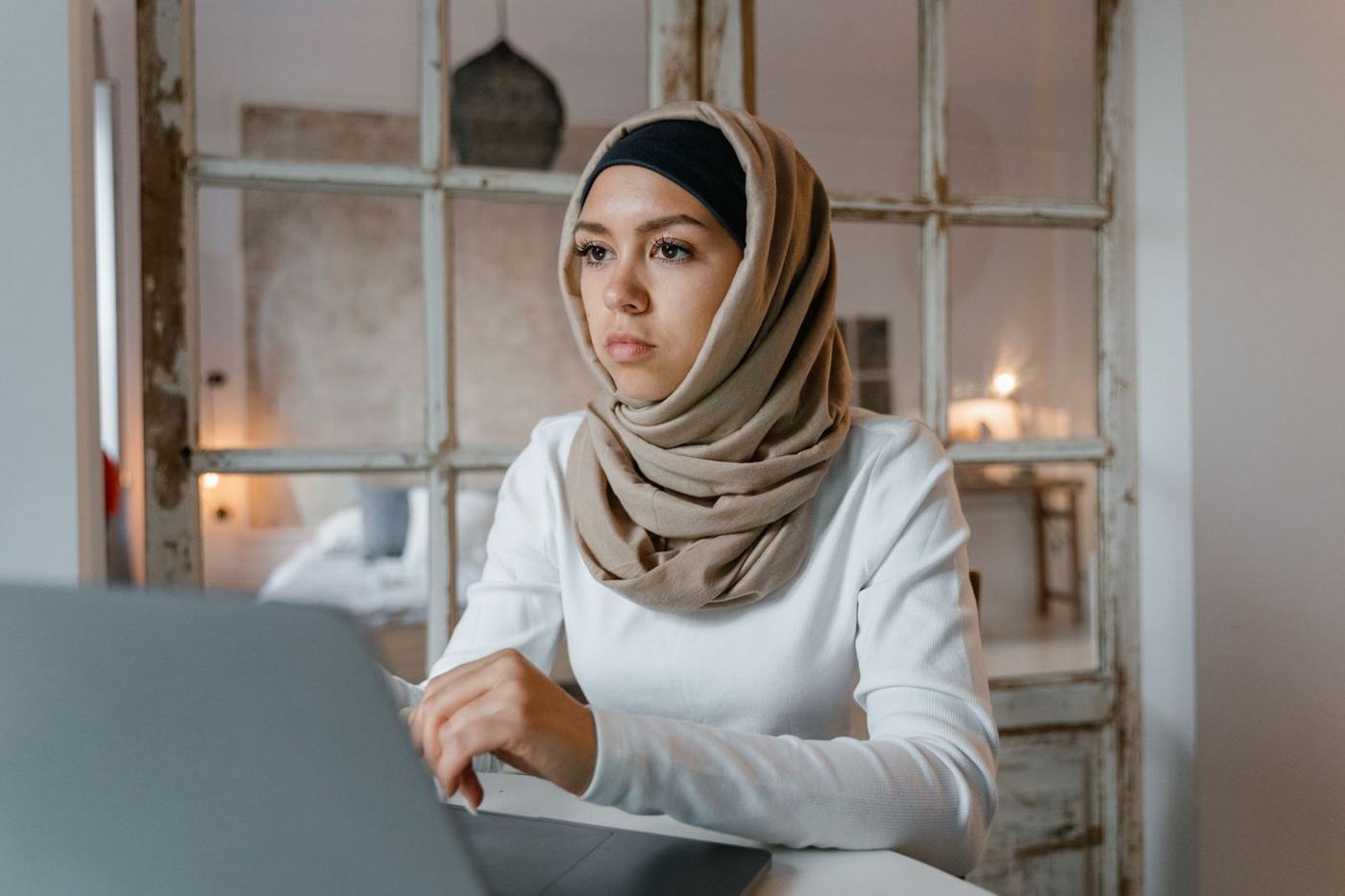 شابة بالحجاب تعمل على حاسوب محمول في المنزل