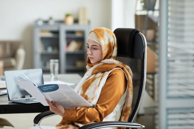 امرأة بحجاب بني تقرأ مستندًا على مكتبها