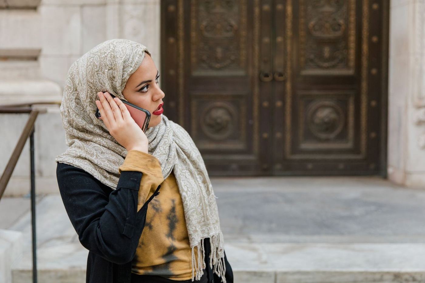 امرأة بغطاء الرأس تتحدث في هاتفها في الخارج