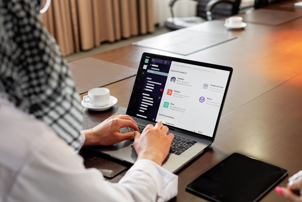 A man in a checked headscarf typing on a laptop at a meeting table