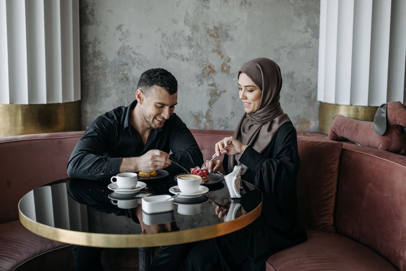 A man and a woman in a hijab sitting at a round table in a lounge, looking at a paper together
