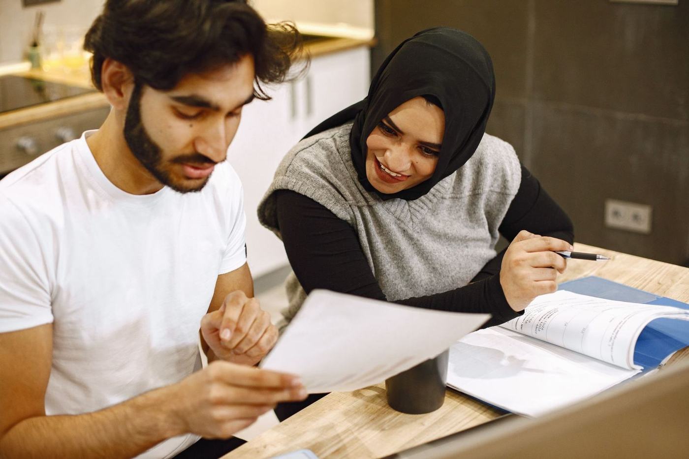 A woman in a hijab and a man sitting at a table at home, going through papers together