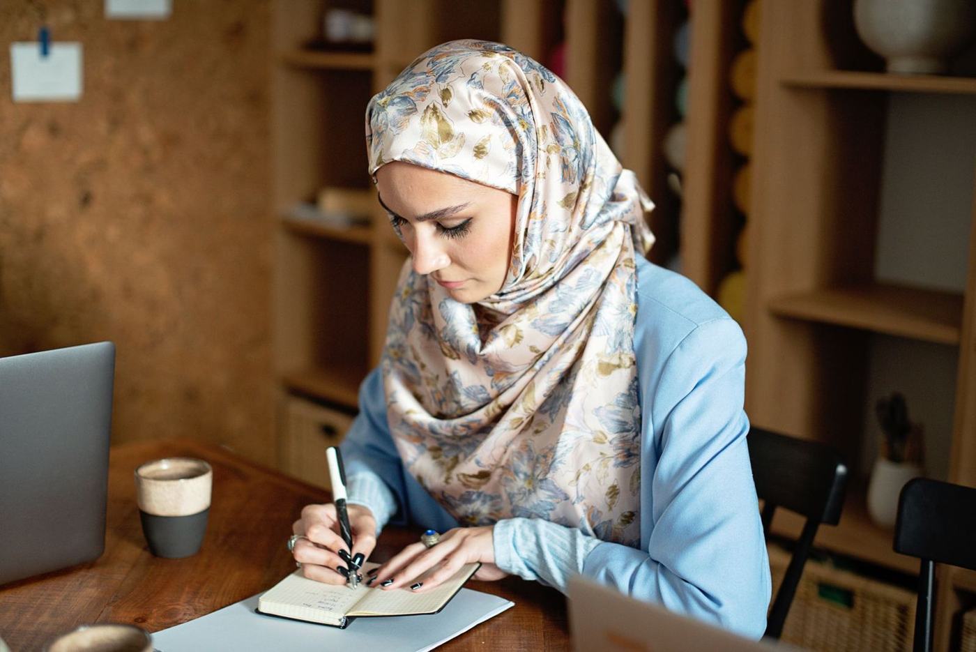 امرأة بحجاب منقوش تكتب في دفتر على مكتب