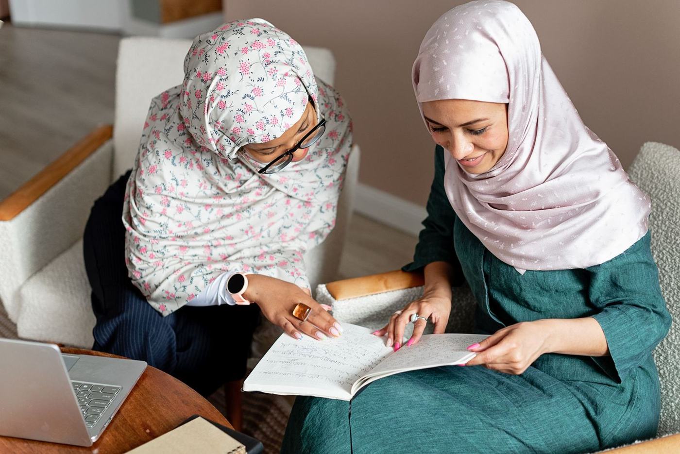 امرأة كبيرة في السن وامرأة أصغر منها بغطاء الرأس تراجعان مستندًا معًا في المنزل