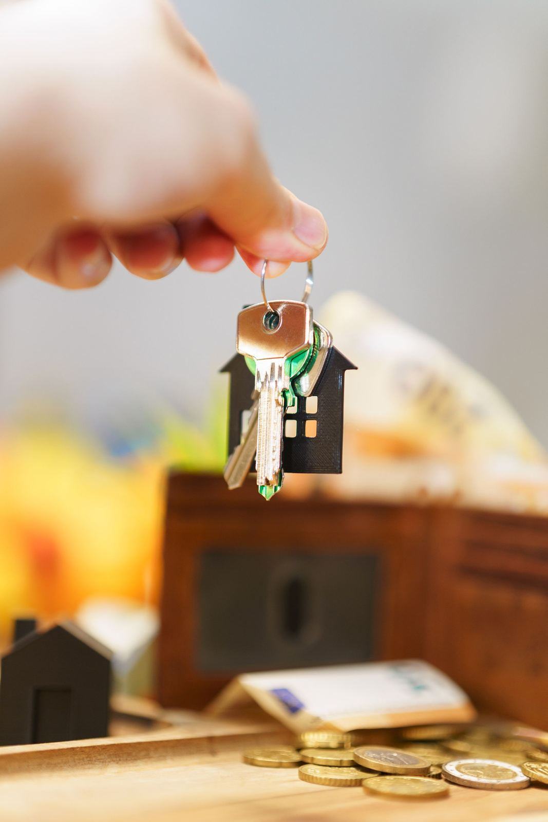 Hand holding house keys above a desk with coins and banknotes