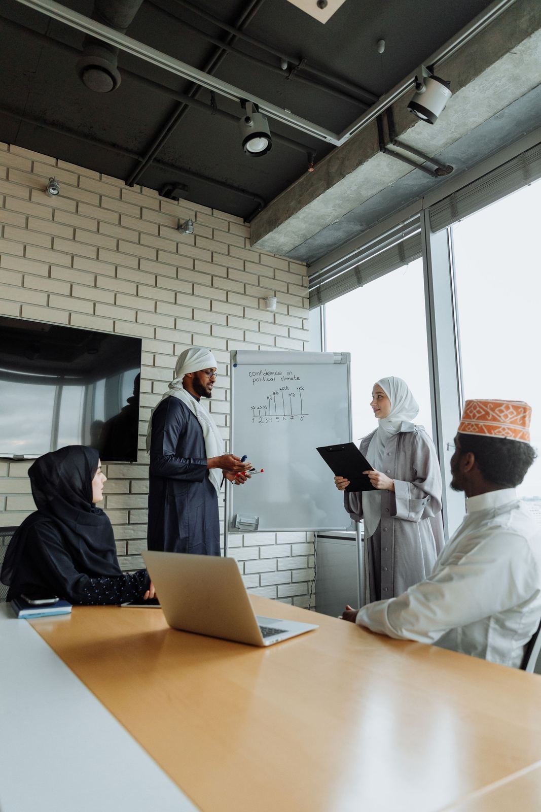 Colleagues in kandura and hijab in a meeting room with a presenter at a whiteboard