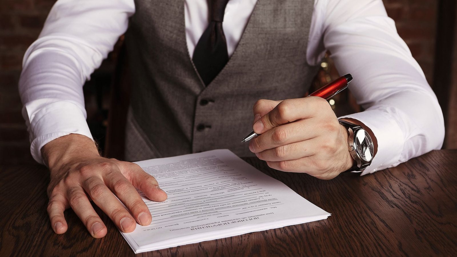Man in a waistcoat and tie signing an affidavit with a pen at a desk