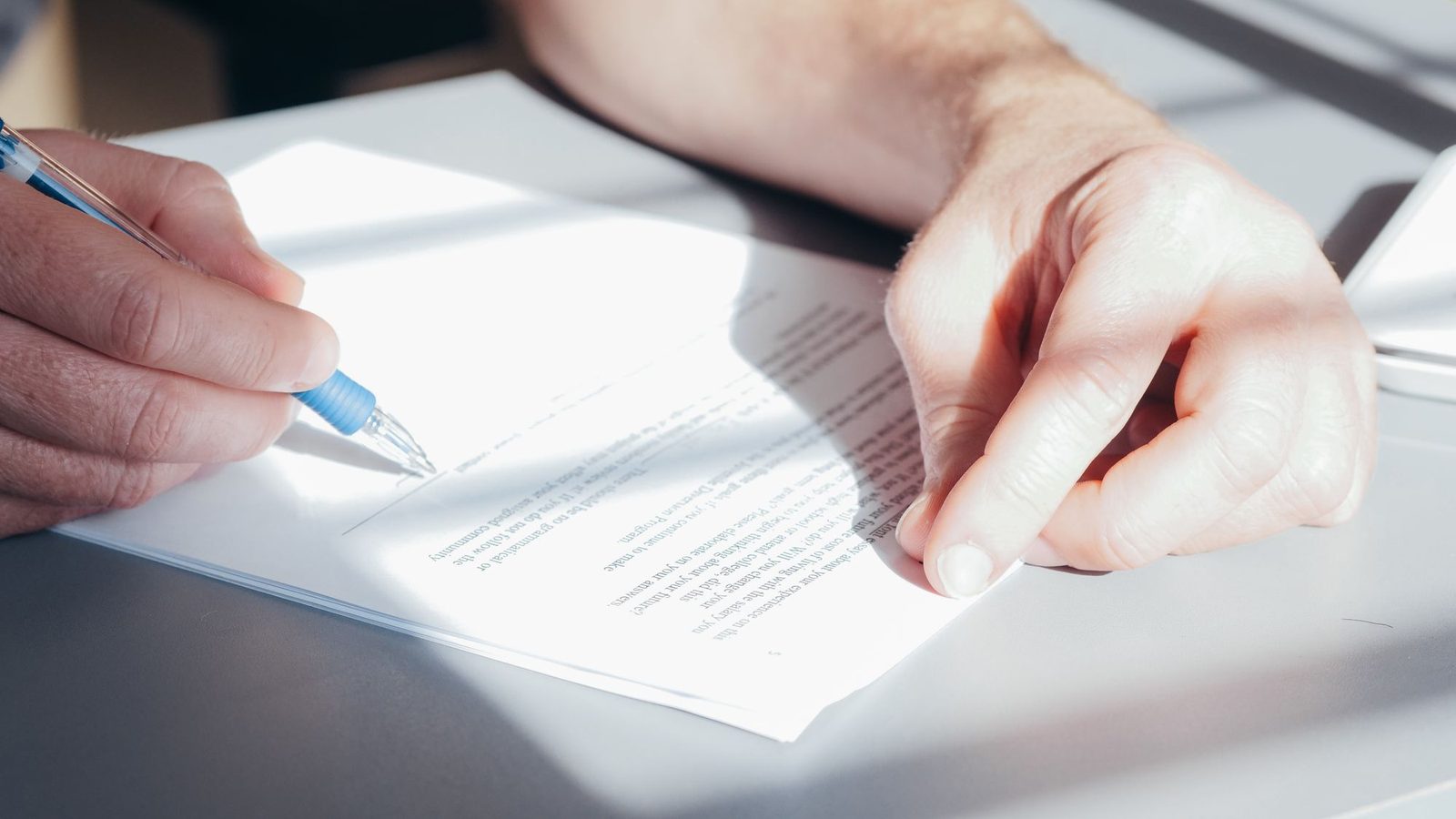 Hands signing a document with a blue pen on a desk, will format UAE