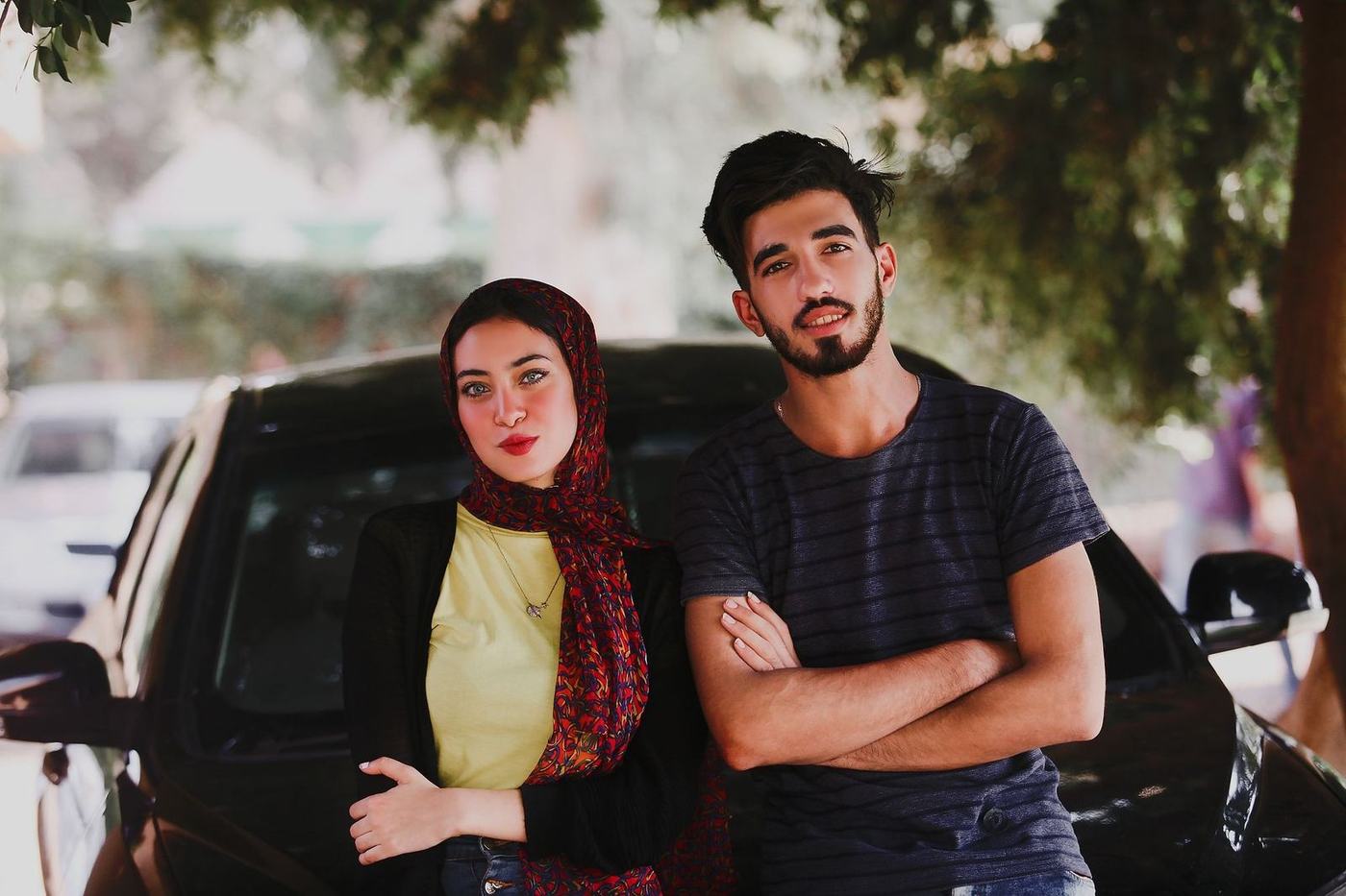 Young Arab couple, the woman in a hijab, standing in front of their car