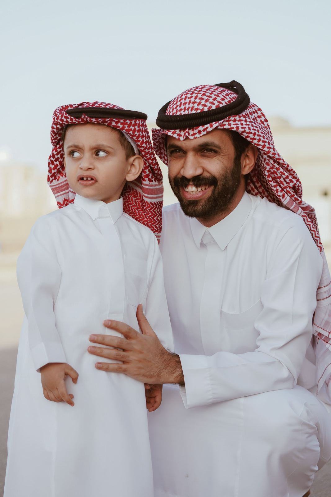 Father in a white thobe and red ghutra with his young son dressed the same way